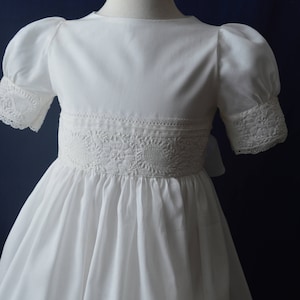 May include: A white dress with puffed sleeves and lace trim. The dress has a round neckline and a full skirt.
