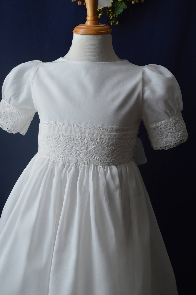 May include: A white dress with puffed sleeves and lace trim. The dress has a round neckline and a full skirt.