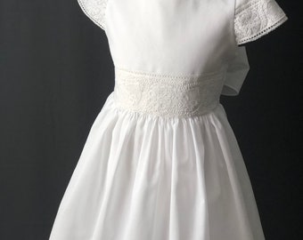 Vestido de comunión para niña, confeccionado a mano con fino algodón suizo y adornado con bordados de obra blanca.