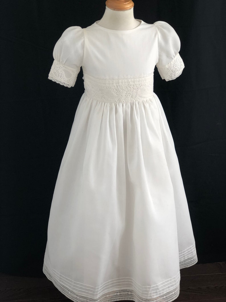 May include: White dress with lace trim and puffed sleeves. The dress has a round neckline and a full skirt.