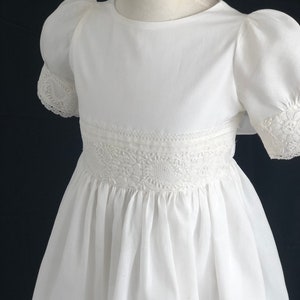 May include: White dress with puffed sleeves and lace trim. The dress has a round neckline and a gathered skirt.