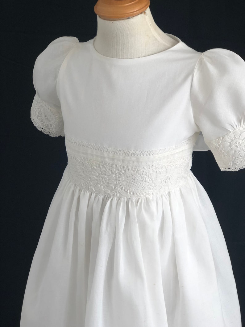 May include: White dress with puffed sleeves and lace trim. The dress has a round neckline and a gathered skirt.