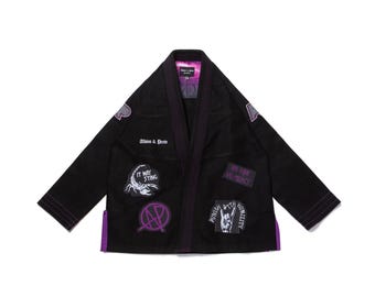 May include: Black martial arts gi with purple trim and patches. Patches include text that says "It May Sting", "No Pain No Mercy", and "Punish with Humility". The gi also has a purple interior lining and the brand name "Alamo & Preto".