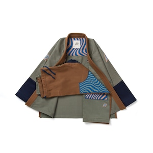 Op de afbeelding: Olijfgroen vechtsportuniform met bruine biezen en marineblauwe accenten. Het uniform bestaat uit een jas en een broek. De jas heeft een golfpatroon in blauw en beige. Het uniform heeft een logopatch.