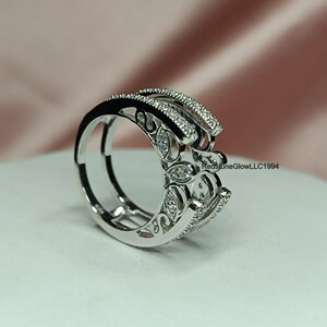 Puede incluir: Un anillo de plata con un dise&ntilde;o delicado e intrincado con peque&ntilde;as piedras transparentes. El anillo tiene una banda doble y est&aacute; sobre un fondo blanco.