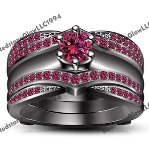 May include: A three-piece black ring set with a large pink gemstone in the center. The ring is adorned with smaller pink gemstones around the band.
