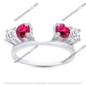 May include: A silver ring with a unique design, featuring two round, vibrant red gemstones and two smaller, clear gemstones. The ring's band curves gracefully, creating an elegant and eye-catching piece of jewelry.