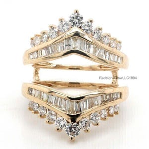 May include: A gold ring with a V-shaped design, featuring a row of baguette diamonds on each side and a row of round diamonds on the bottom. The ring is designed to be worn as a wedding band enhancer.