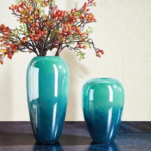 Può includere: Una tazza di ceramica bianca con manico nero e la scritta "But First, Coffee" in grassetto nero. La tazza è appoggiata su una superficie di legno. La tazza è alta circa 10 cm.