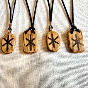 Peut inclure: Quatre colliers pendentifs en bois avec des cordons noirs. Chaque pendentif a une forme différente, avec un symbole sombre en forme d'étoile sculpté dans le bois. Les pendentifs sont de différentes nuances de marron et de beige.