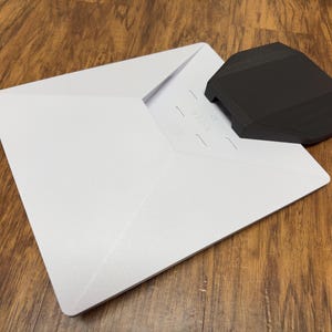 May include: A white envelope with a black plastic envelope sealer on top. The sealer has a textured surface and a small handle.