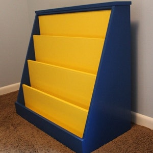 May include: A blue and yellow wooden bookshelf with four shelves. The bookshelf is angled and has a simple design.