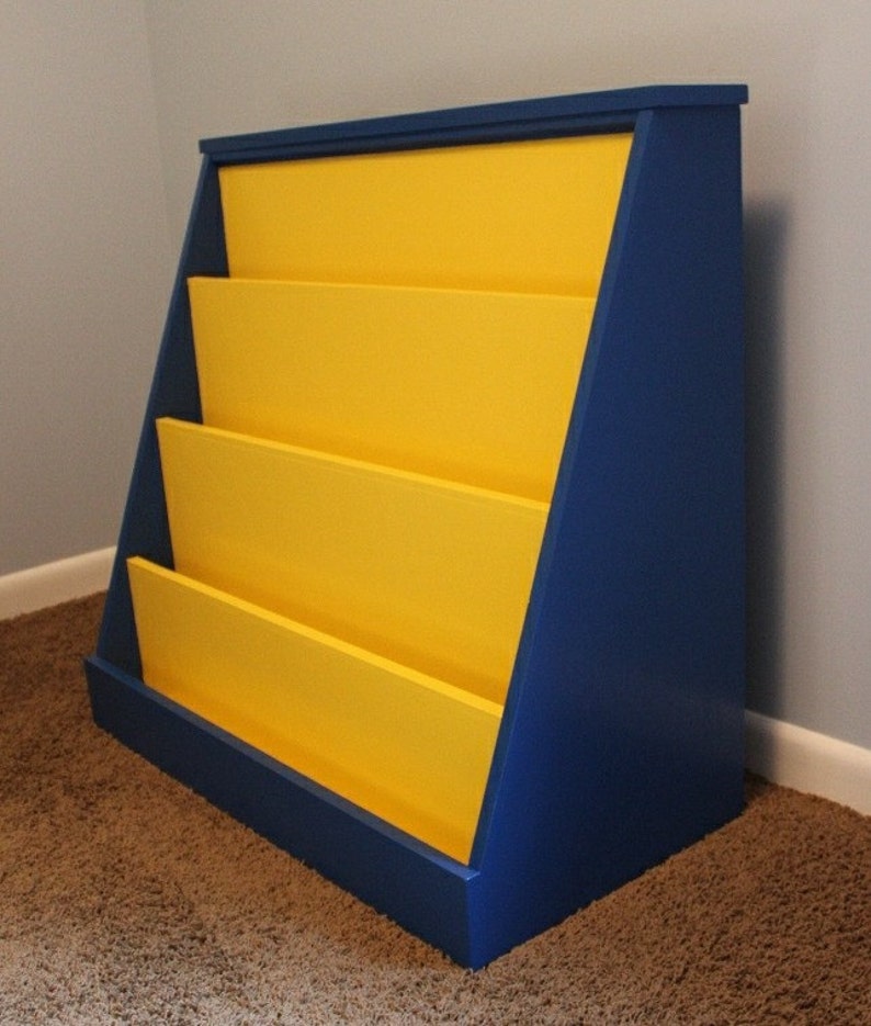 May include: A blue and yellow wooden bookshelf with four shelves. The bookshelf is angled and has a simple design.
