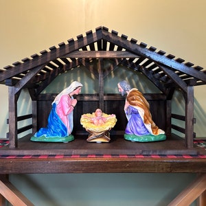 May include: A wooden nativity scene with a brown stained finish. The figures are made of painted plaster and depict Mary, Joseph, and the baby Jesus in a manger.