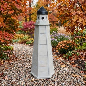 May include: A tall, hexagonal lighthouse-shaped birdhouse with a light gray, weathered wood finish and a dark, pointed roof. The structure features a small circular opening near the top, designed for birds to enter, and a sturdy, multi-paneled base.