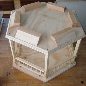 Peut inclure: Un gazebo octogonal en bois avec une base en contreplaqu&eacute; et une balustrade autour du p&eacute;rim&egrave;tre. Le gazebo est non fini et a une couleur bois naturelle.