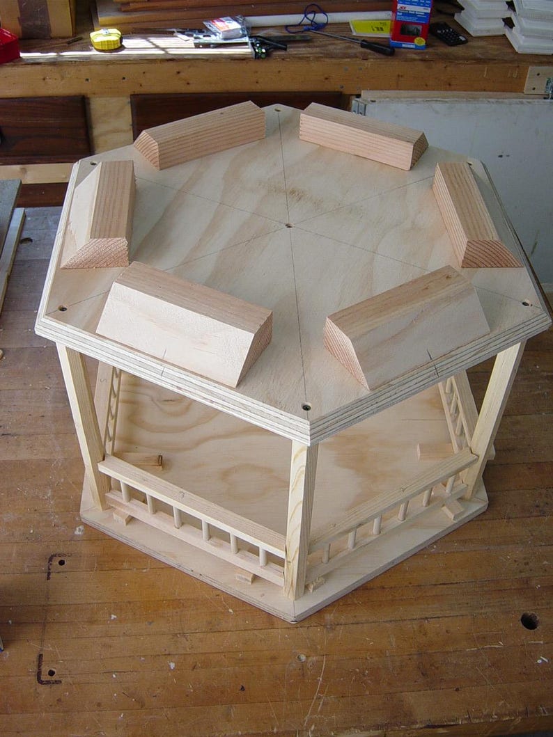 Peut inclure: Un gazebo octogonal en bois avec une base en contreplaqu&eacute; et une balustrade autour du p&eacute;rim&egrave;tre. Le gazebo est non fini et a une couleur bois naturelle.