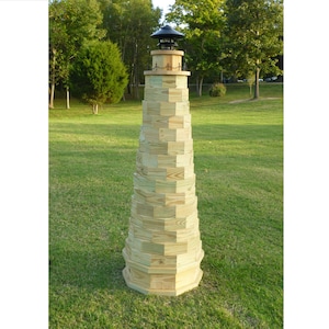 May include: A wooden lighthouse-shaped garden decoration with a black metal lantern on top. The lighthouse is made of stacked wooden planks and is standing on a green grassy lawn.