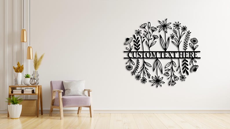 May include: Black metal floral wall art with the text "CUSTOM TEXT HERE" in a circular design. The art features various flower and leaf silhouettes. The wall art is mounted on a white wall.