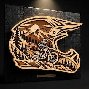 May include: A multi-layered wooden wall art piece shaped like a motocross helmet, featuring a laser-cut scene of a rider on a dirt bike navigating a mountain trail with pine trees, a sun, and birds, mounted on a charred black wooden panel.