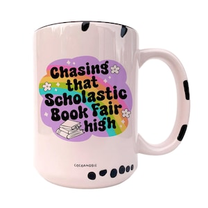 May include: White ceramic mug with a black rim and handle. The mug has a black and white polka dot pattern around the bottom. The mug features a rainbow design with the text "Chasing that Scholastic Book Fair high" and a stack of books.