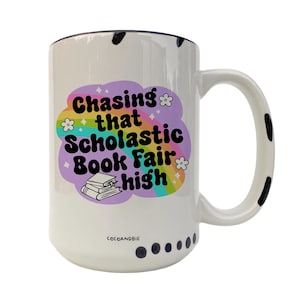 May include: White ceramic mug with a black rim and black polka dots around the bottom. The mug features a rainbow design with the text "Chasing that Scholastic Book Fair high".