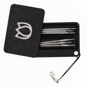 May include: Black case with a white logo and a set of silver knitting needles. The case is open, revealing multiple needles in two compartments. A black cord with a silver clasp is attached to the case.