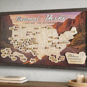 May include: Wooden map of the United States with a dark brown frame, featuring a road and mountain backdrop. The map is labeled "National Parks - Explore the Outdoors" and includes small tree icons and park names. A welcome sign is also included.