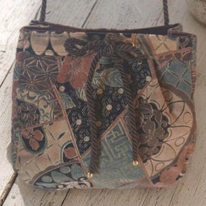 May include: A patchwork fabric handbag with a drawstring closure and a shoulder strap. The bag features a variety of floral and geometric patterns in shades of brown, beige, and blue. The drawstring is a dark brown rope.