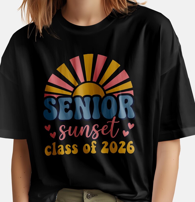 May include: Black t-shirt featuring a colorful graphic design. The design includes the words "SENIOR sunset class of 2026" in a retro font, with a sunset and heart accents. The shirt is made of a soft material.