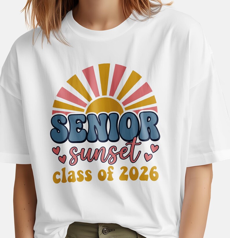 May include: White t-shirt featuring a retro design with the words "SENIOR sunset class of 2026." The design includes a stylized sunset in shades of pink, yellow, and blue, with heart accents. The shirt is a casual, comfortable style.