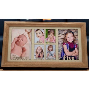 May include: A wooden picture frame with eight openings for photos. The frame has a light brown finish and the openings are labeled with the words "Newborn", "One", "Two", "Three", "Four", and "Five".