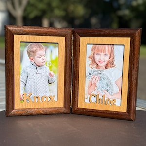 May include: A hinged, double photo frame with a dark brown wooden border and a light brown interior. The frame holds two photos, one of a young boy and the other of a young girl holding a rabbit. The names "Knox" and "Chloe" are cut out at the bottom.