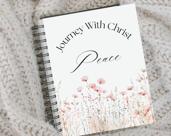 May include: A white journal with a black spiral binding. The cover features the text "Journey With Christ Peace" in black script font and a watercolor illustration of pink wildflowers.