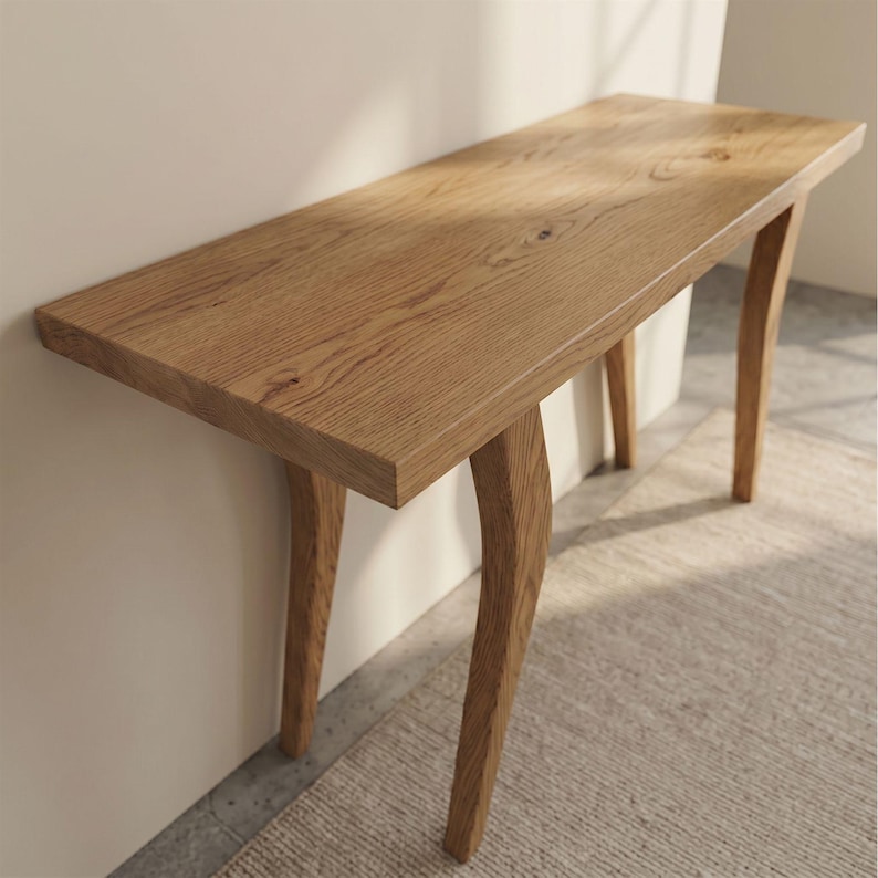 Op de afbeelding: Een lichtbruine houten consoletafel met een rechthoekig blad en gebogen poten. De tafel is gemaakt van hout en heeft een natuurlijke afwerking. De tafel is ongeveer 122 cm lang, 30 cm breed en 76 cm hoog.