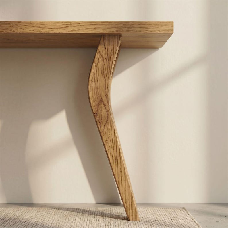 Op de afbeelding: Close-up van een lichte eikenhouten tafel met een gebogen pootontwerp. Het rechthoekige tafelblad wordt ondersteund door een enkele, elegant gebogen poot. De houtnerf is zichtbaar en voegt textuur en warmte toe aan het stuk. Een modern meubel.