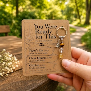 May include: A keyring featuring a silver-tone ring, a letter M charm, and three beads: a brown tiger's eye, a clear quartz, and a yellow citrine. It is attached to a tan card with the text You Were Ready for This and descriptions of the stones.