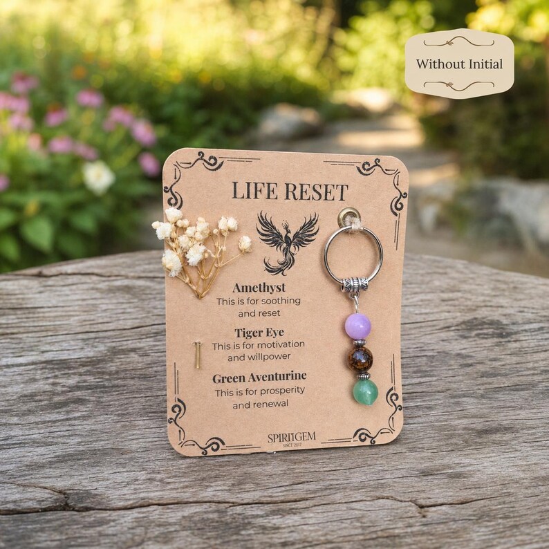 May include: A keychain with a card that reads "LIFE RESET." The keychain has a silver ring and three gemstone beads: amethyst, tiger eye, and green aventurine. The card also has text that describes the properties of each stone.