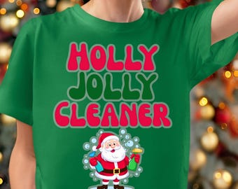 May include: A green short-sleeved t-shirt featuring the text HOLLY JOLLY CLEANER in red and green letters. Below the text is a graphic of Santa Claus wearing a red suit and hat, holding two spray bottles surrounded by floating bubbles.