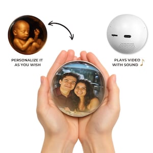 Op de afbeelding: Een heldere, bolvormige fotoweergave in handen, met een foto van een stel. De weergave is verbonden met een witte bol met poorten en een luidspreker, met de tekst "PLAYS VIDEO WITH SOUND." Een andere afbeelding toont een foetus met de tekst "PERSONALIZE IT AS YOU WISH."