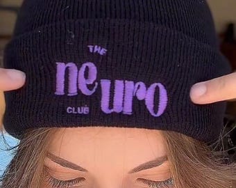 May include: A black beanie with the text "THE neuro CLUB" in purple. The same text is also on a gray sweatshirt. The image shows a person wearing the beanie and sweatshirt.