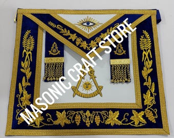 Puede incluir: Delantal masónico con centro blanco, bordes azules y bordados dorados. El delantal presenta símbolos como un ojo que todo lo ve, un sol y herramientas. El texto "MASONIC CRAFT STORE" es visible.