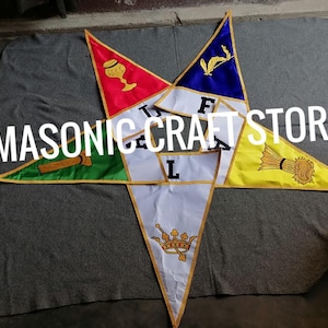 Può includere: Una collezione di bandiere triangolari colorate disposte a forma di stella. Ogni bandiera presenta un colore e un simbolo diversi, tra cui un calice, un covone di grano e una corona. Il testo "MASONIC CRAFT STORE" è sovrapposto all'immagine.