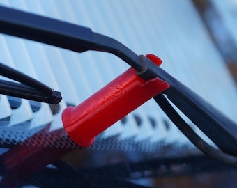Könnte beinhalten: Nahaufnahme einer Autoscheibe mit schwarzen Scheibenwischern und roten Wischerblatt-Schutzvorrichtungen. Die Wischer sind vor einem blau-weißen Hintergrund positioniert, was auf ein Fahrzeugpflege- oder Automobilprodukt hindeutet.