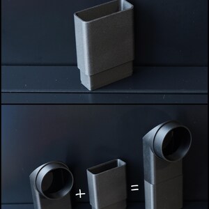 May include: A dark gray, rectangular object with a smaller rectangular base. The image shows how the object can be combined with a curved, cylindrical piece to form a right-angle connector. The objects are on a dark surface.