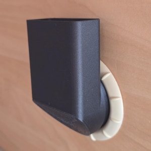 May include: A black, rectangular object with a curved, off-white base. The object appears to be a holder or container, possibly for a phone or other small item. The design is modern and minimalist.