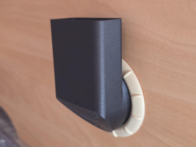 May include: A black, rectangular object with a curved, off-white base. The object appears to be a holder or container, possibly for a phone or other small item. The design is modern and minimalist.