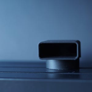 May include: A close-up shot of a black, rectangular object with rounded corners, mounted on a small, circular base. The object has a hollow interior and is set against a blurred blue background.