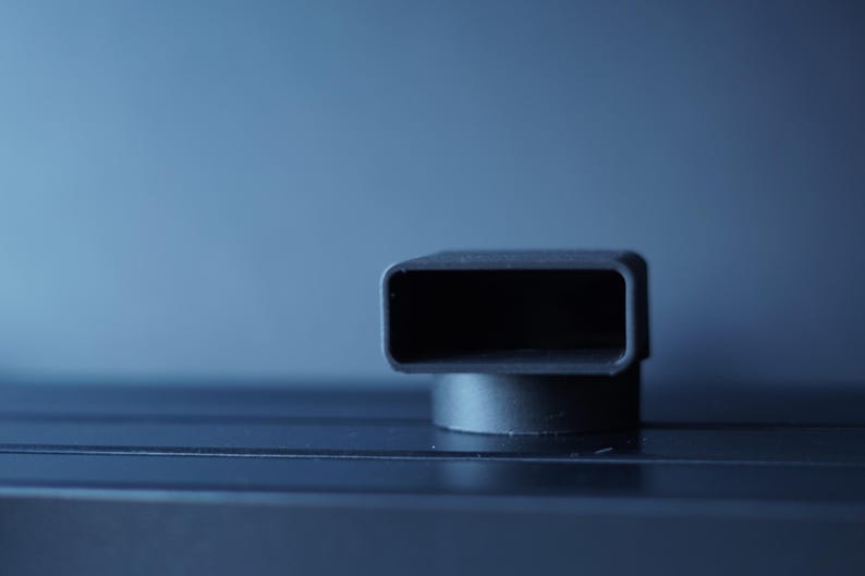 May include: A close-up shot of a black, rectangular object with rounded corners, mounted on a small, circular base. The object has a hollow interior and is set against a blurred blue background.