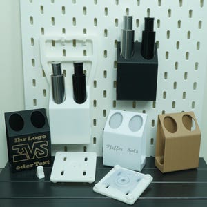 May include: A collection of various pen holders and mounting accessories in black, white, and tan. Some holders have two openings, while others have a single opening. One holder has the text "Ihr Logo EVS oder Text".